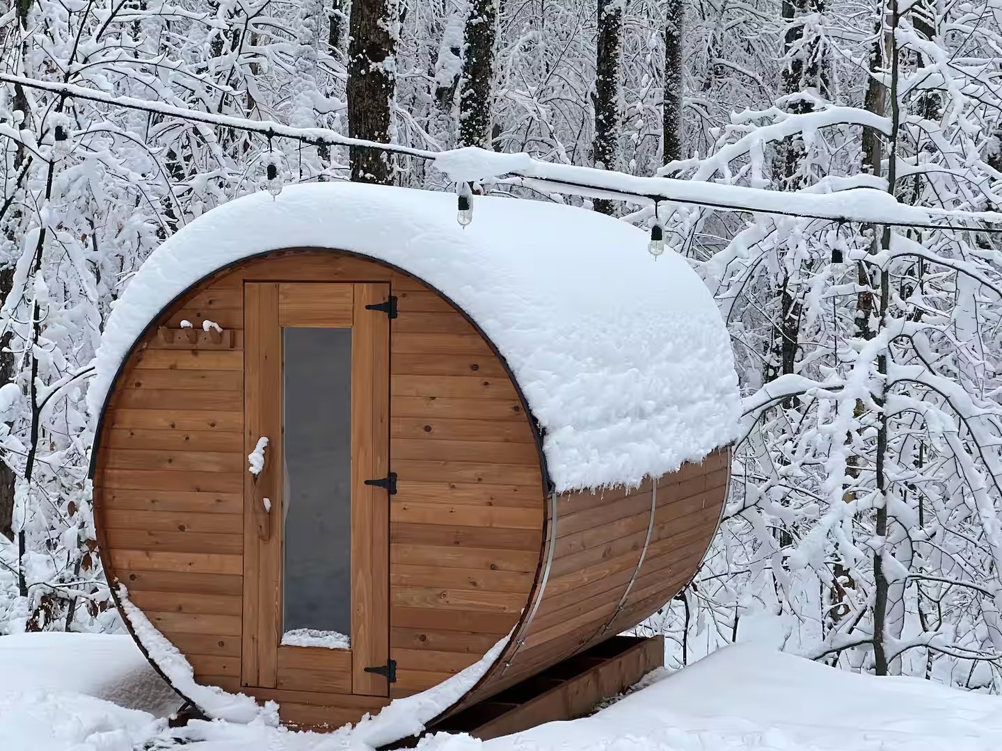 Outdoor barrel sauna covered in snow, made of cedar wood, installed in a winter forest setting in Canada