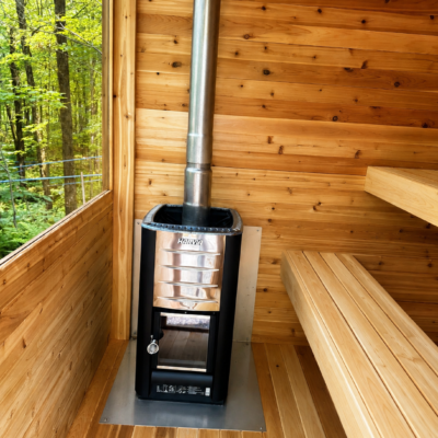 inside moderna sauna with wood stove | SaunaSpa Interior of a cedar sauna with a Harvia wood-burning stove, clean wooden benches, and a large window overlooking a green forest.