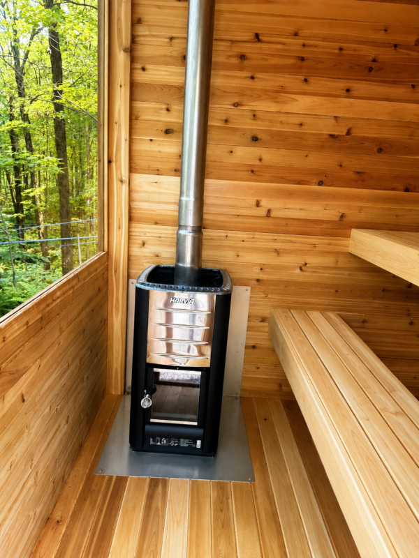 inside moderna sauna with wood stove | SaunaSpa Interior of a cedar sauna with a Harvia wood-burning stove, clean wooden benches, and a large window overlooking a green forest.